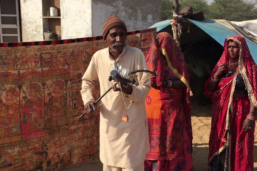 Man with traditional instrument and women in bright ethnic clothes of Rajasthan.