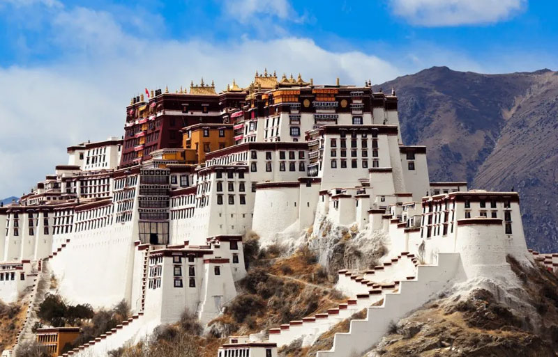 Potala Palace's massive white walls and red upper sections rising from rocky hillside against clear mountain backdrop.