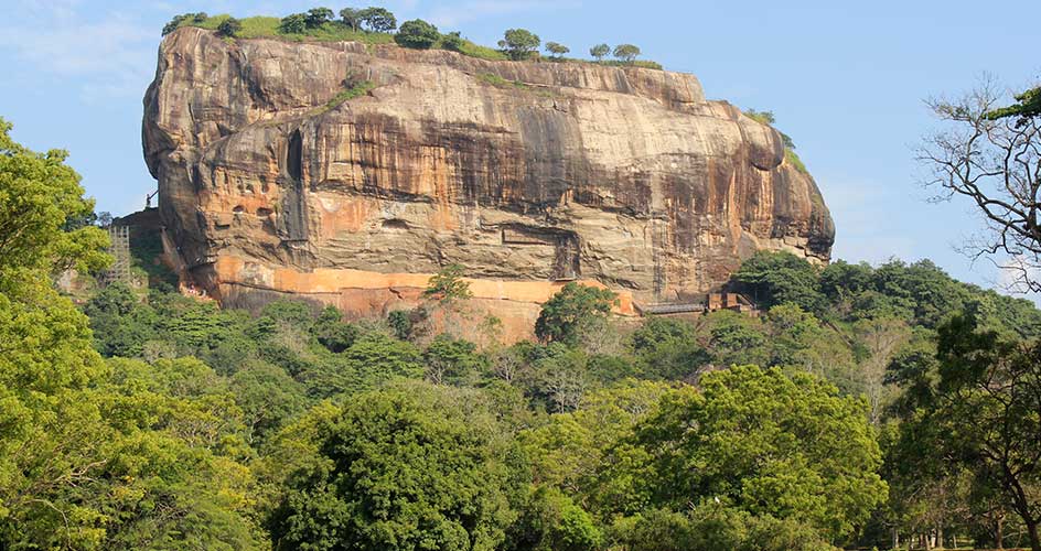 Massive rock fortress with vertical cliff face rising above surrounding jungle vegetation