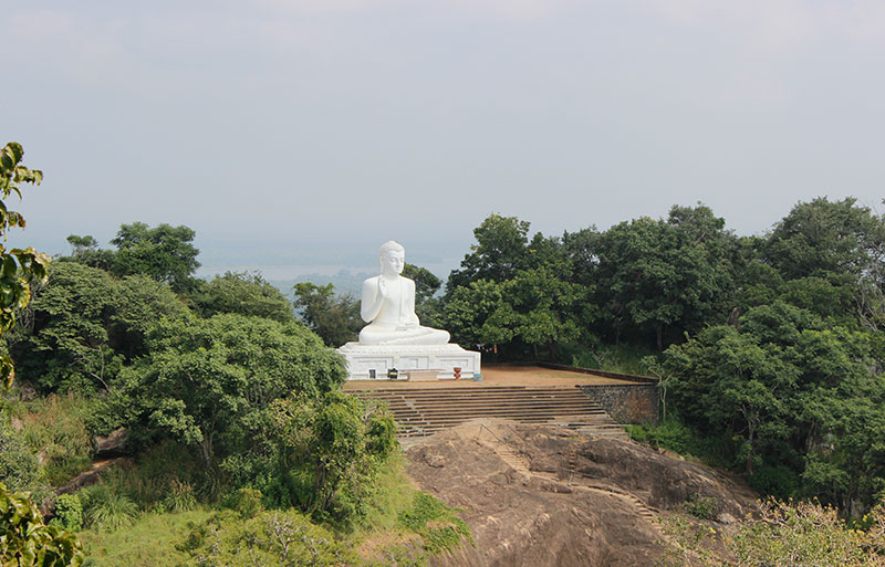 White Buddha statue in meditation pose on hillside platform overlooking misty valley landscape