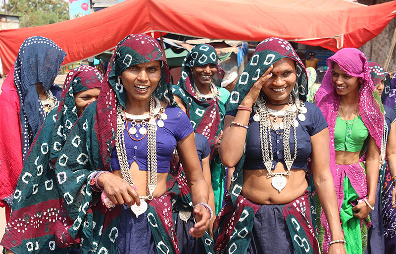 Joyful women in traditional attire with silver jewelry dancing under red canopy