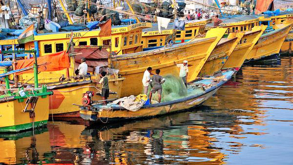 Colorful yellow and blue fishing boats docked at an Indian harbor with fishermen working
