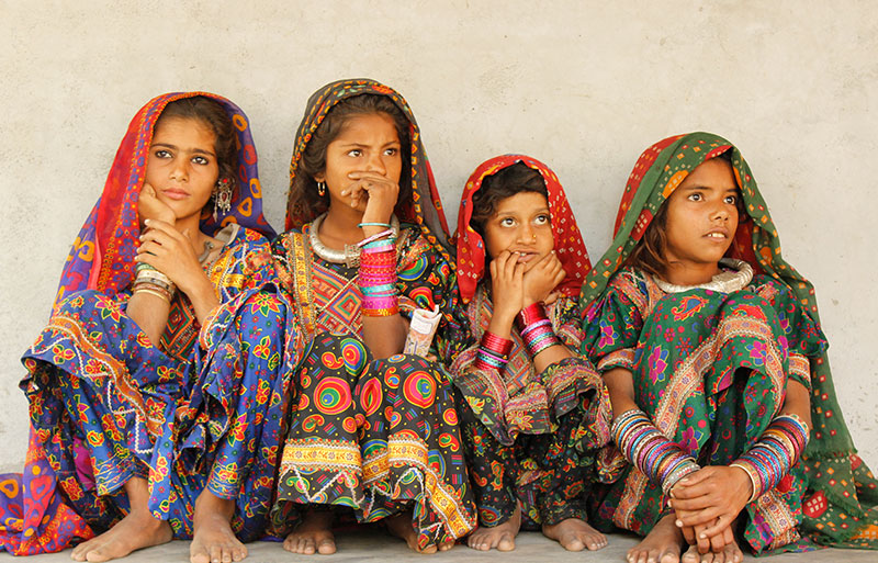 Four young girls in vibrant traditional embroidered dresses and colorful headscarves sitting together
