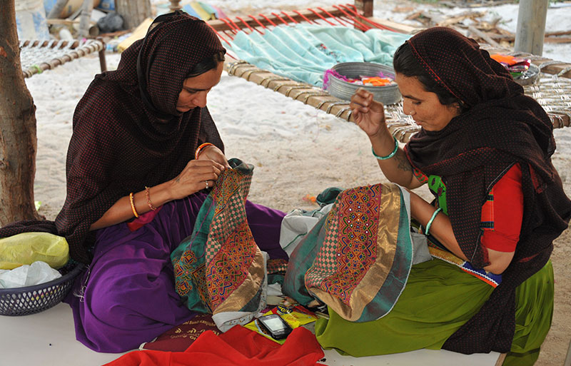 Two women doing detailed embroidery work on colorful fabric outdoors