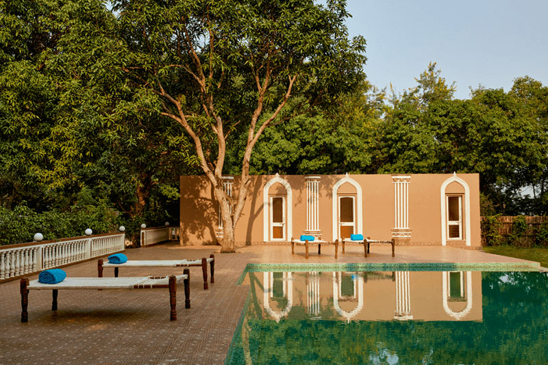 View of poolside with terracotta wall and white arched windows with water reflections.