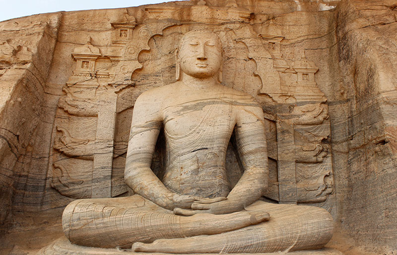 Large seated Buddha carved in meditation pose within natural rock alcove with architectural details