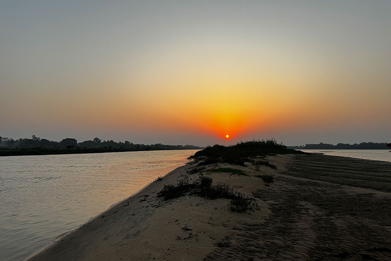 Silhouetted shoreline and gradient sky on an orange sunset over river delta.