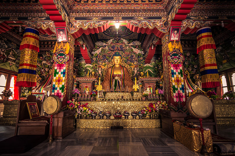 Ornate Buddhist temple interior with golden Buddha statue on altar, draped flags and decorative pillars — Footprints of Buddha Tour.