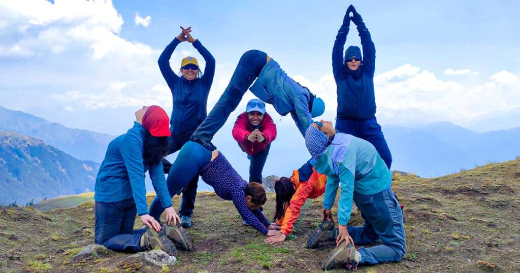Hiking group writing Yoga with their bodies in colorful outdoor apparel on mountain top landscape.