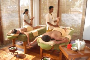 Two massage therapists offer Ayurvedic oil synchronized massage to clients in relaxing spa room.