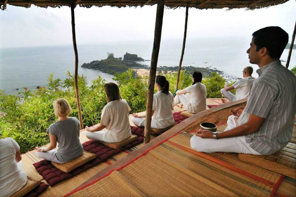 Group meditation session in thatch shelter with scenic view of the coast in the background.